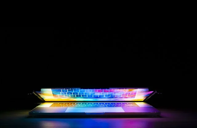 A partially open laptop with colorful backlit keyboard in the dark