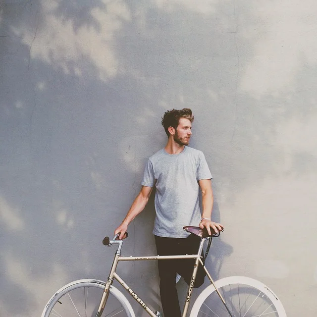 El Blanco Essentials Oversized T Shirt: A man in a grey t-shirt standing with a bicycle