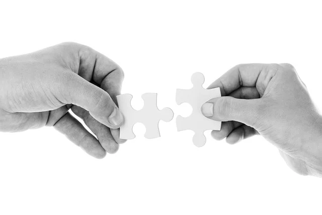 Two hands connecting two puzzle pieces together