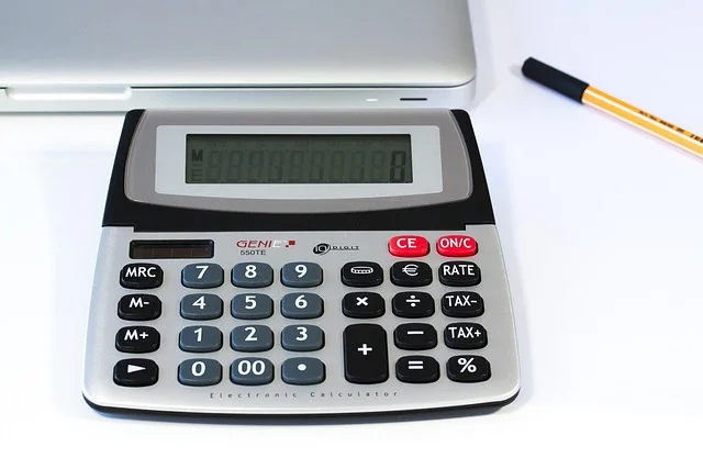 A calculator next to a laptop and a pen