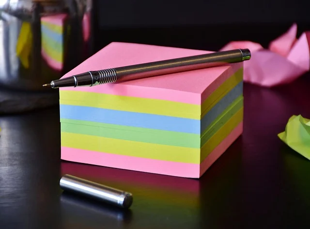 A stack of colorful sticky notes with a metal pen