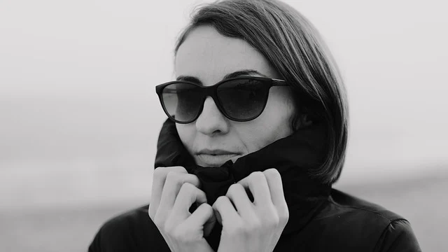 A woman wearing sunglasses and holding up a high jacket collar