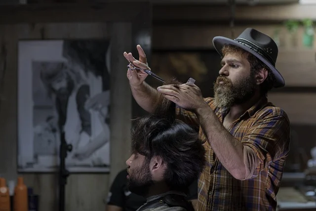 A bearded barber wearing a hat cutting a client's hair