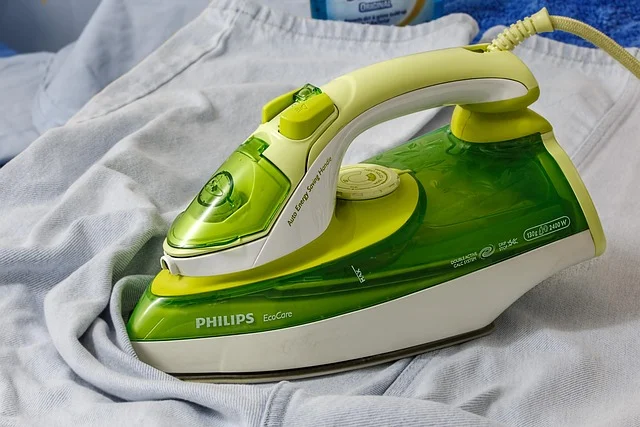 A green steam iron resting on a piece of light blue clothing