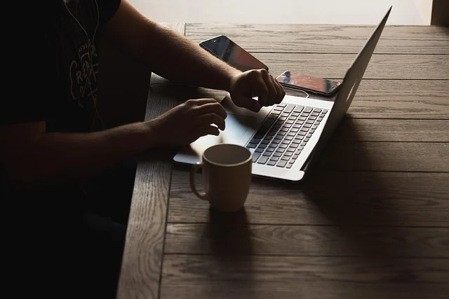 A person working on a laptop with a mug and phones nearby