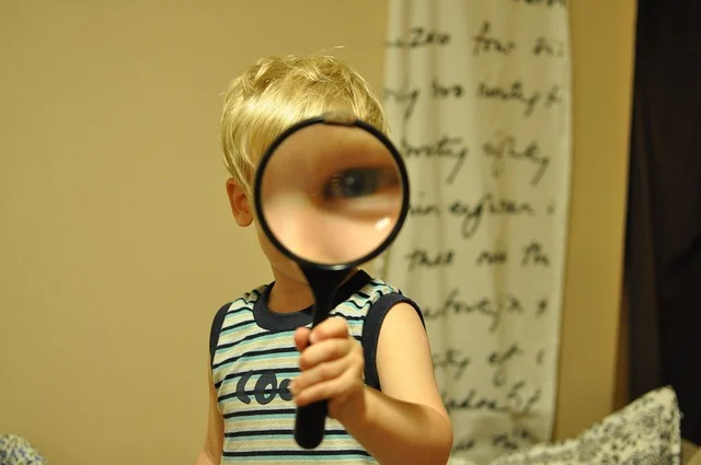 A young boy holding a magnifying glass over his eye