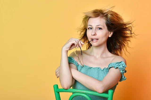 A woman in a green off-the-shoulder top holding glasses