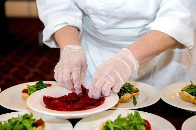 A chef wearing gloves plating food with sliced beets and greens