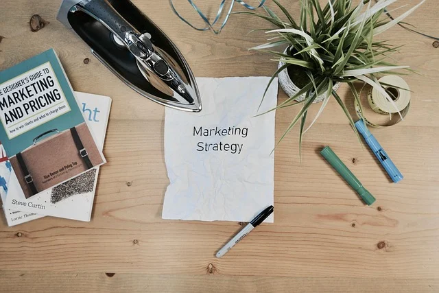Desk with clothing tools, a marketing book, and paper reading Marketing Strategy