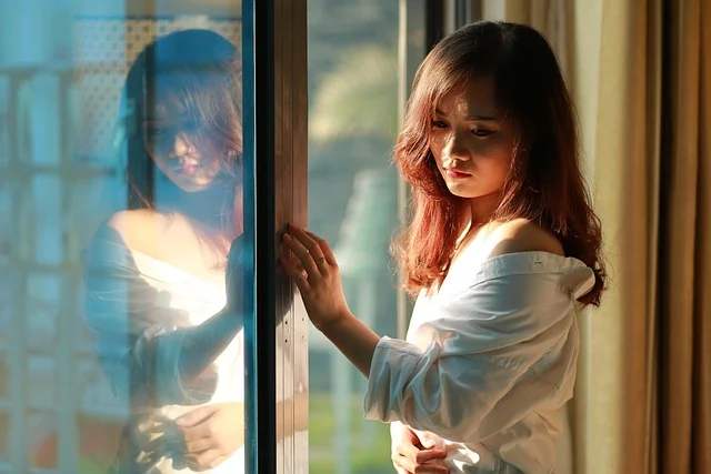 Asymmetric top: A woman wearing an off-the-shoulder white shirt by a window