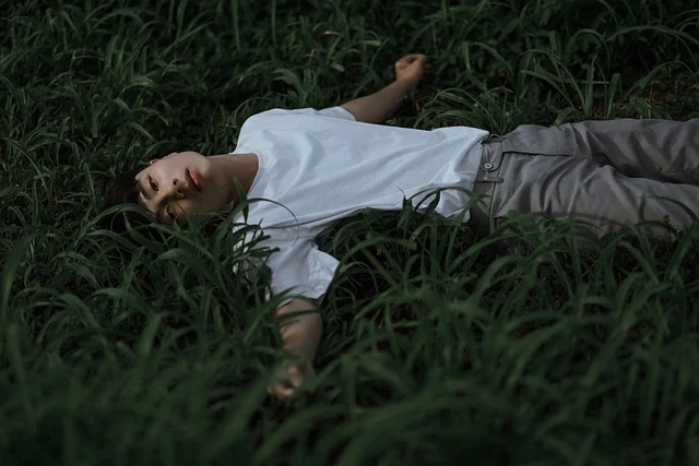 A person lying in grass wearing a plain white t-shirt