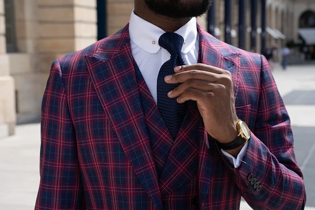 A man wearing a tailored plaid suit adjusting his tie