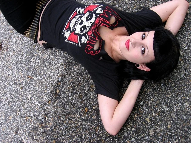 A woman in goth punk attire lying on pavement wearing graphic t-shirt