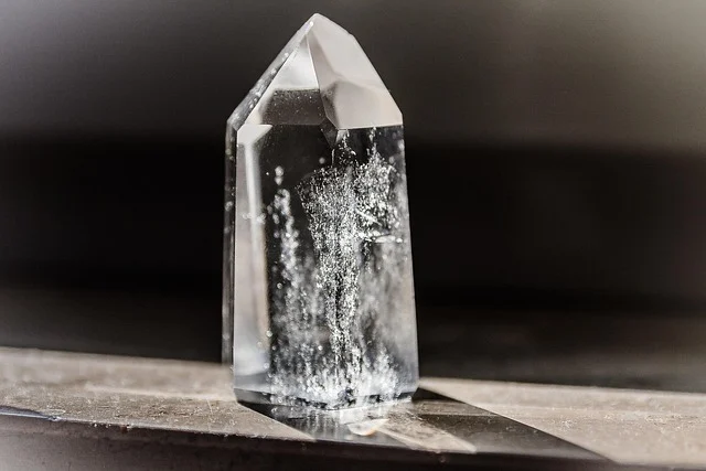 A clear quartz crystal point with internal inclusions standing upright