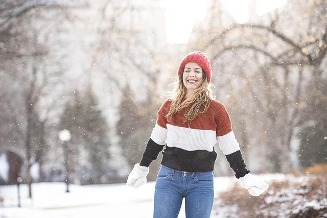 A smiling woman wearing a sweater and blue jeans in winter