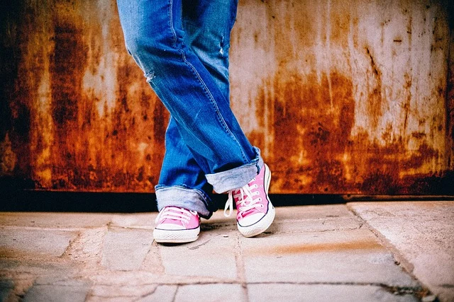 A person wearing blue jeans and pink canvas sneakers