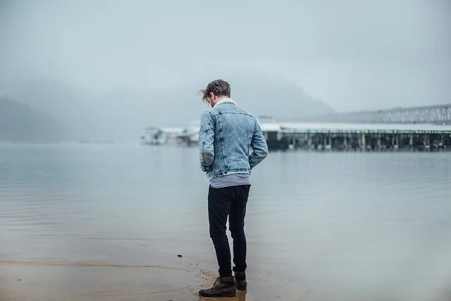 Black jeans men: A man standing by a body of water wearing black jeans