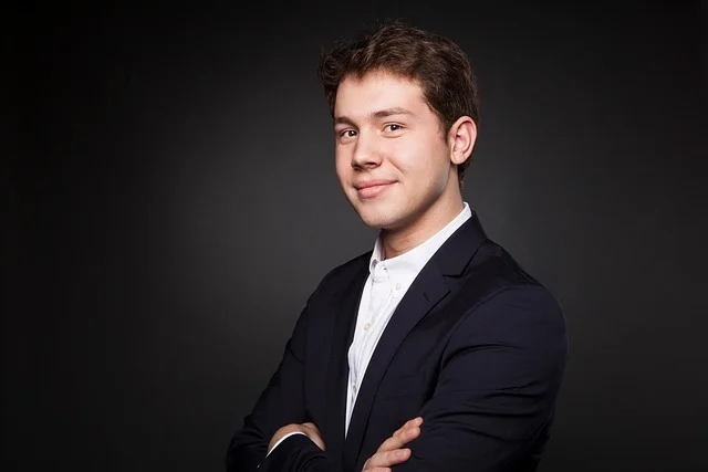 A young man wearing a dark suit jacket and white shirt