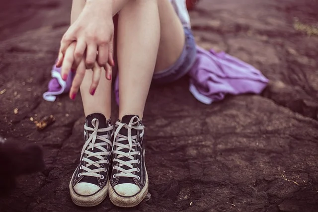 A person sitting outdoors wearing black canvas high-top sneakers