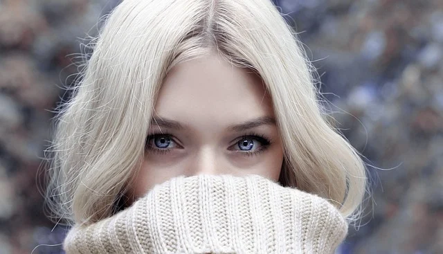 Close-up of a blonde woman covering her lower face with a sweater