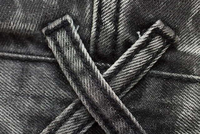 Close-up of crossed belt loops on faded black denim fabric