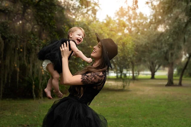 A woman in a black dress holding a toddler in a park