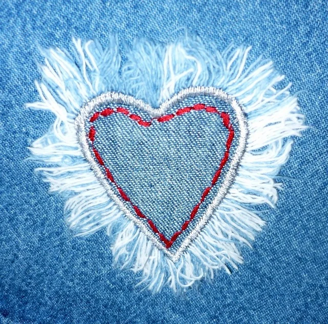 A heart-shaped stitched denim patch with frayed edges on denim fabric