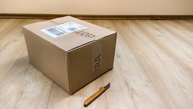 A sealed cardboard shipping box and a utility knife on wooden flooring