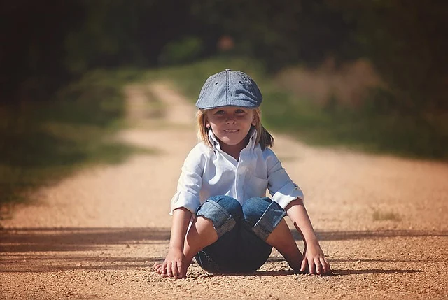 A young child wearing denim jeans and a cap on a dirt path