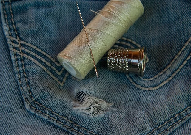 A spool of thread, needle, and thimble on denim fabric