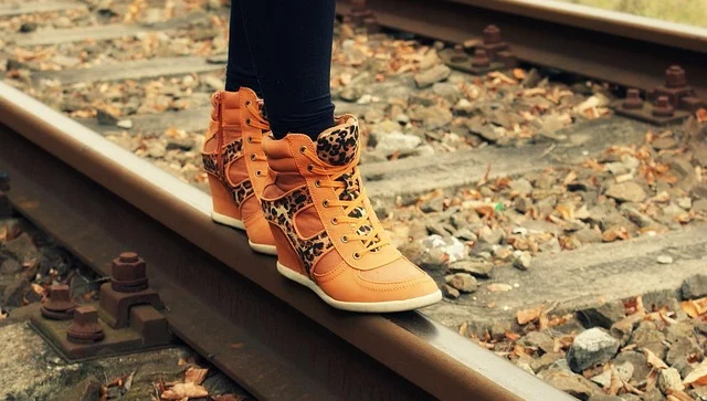 A person wearing orange wedge sneakers walking on railroad tracks