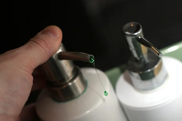 A hand pressing a soap pump dispenser dripping green liquid