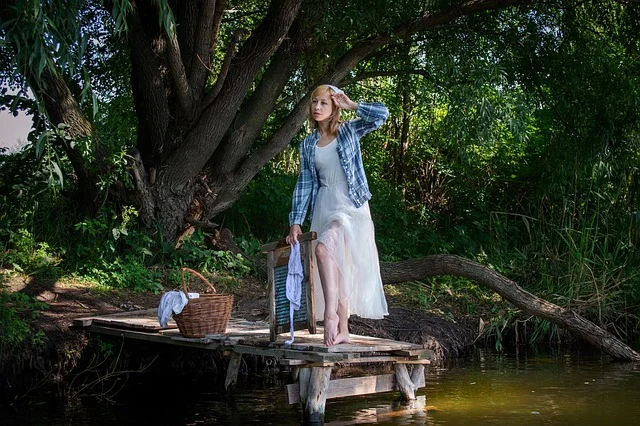 A woman standing on a wooden pier with a washboard and laundry basket
