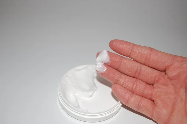 A hand scooping white cream lotion from a tub