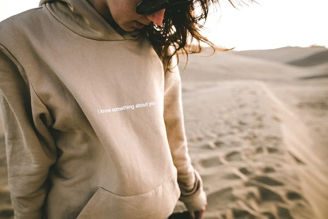 Person wearing a beige oversized hoodie with dark jeans and white sneakers.