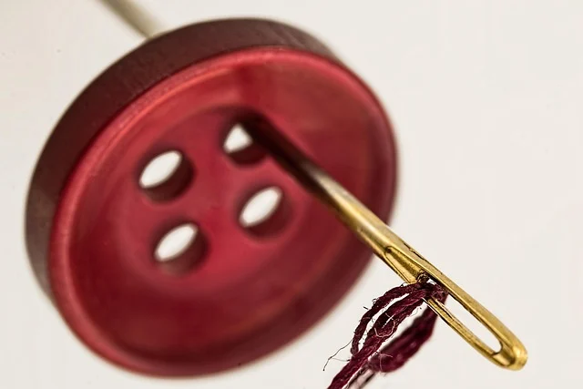A close-up of a red button with a needle and thread