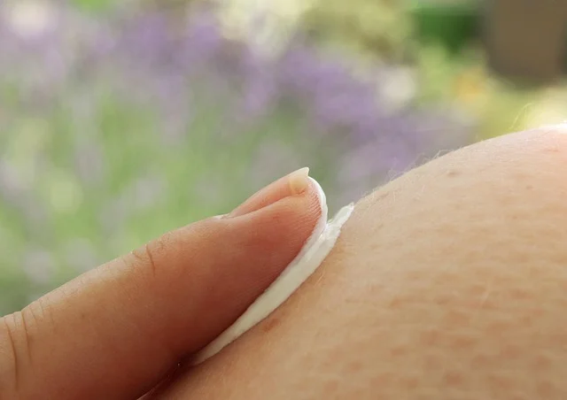 A finger spreading white lotion cream onto skin close up