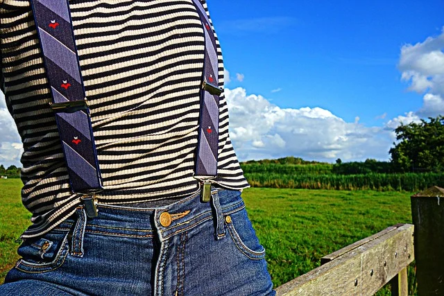 A person wearing a striped shirt, suspenders, and blue jeans outdoors