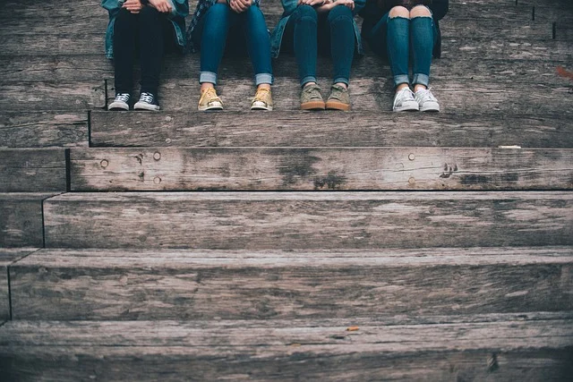 Four people sitting on wooden steps wearing jeans and sneakers