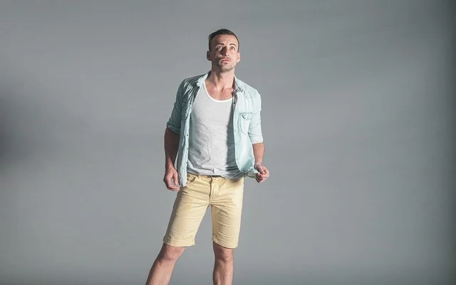 A man in a light blue shirt and yellow shorts posing