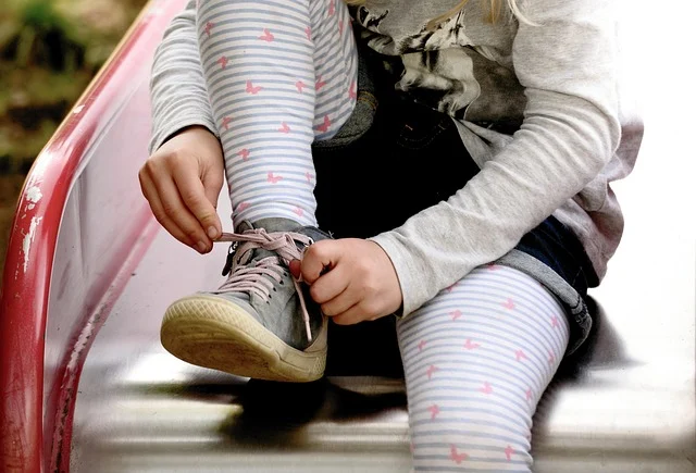 A child tying the laces of a sneaker while outdoors