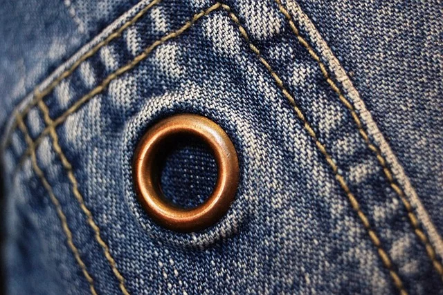 Close-up of blue denim fabric with stitching and a metal grommet