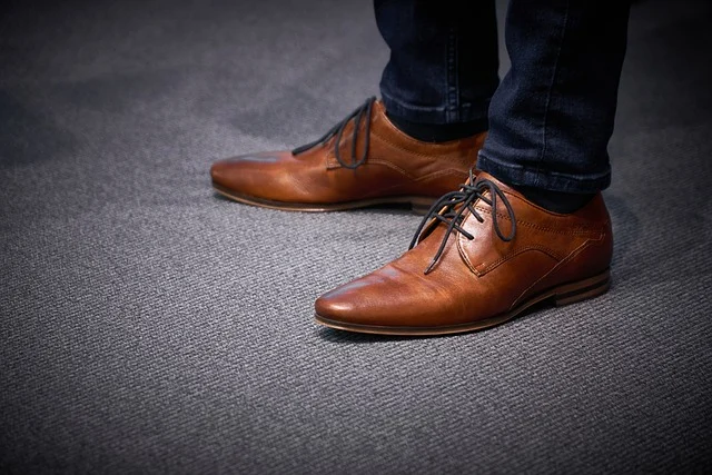 A person wearing brown leather dress shoes with dark blue jeans