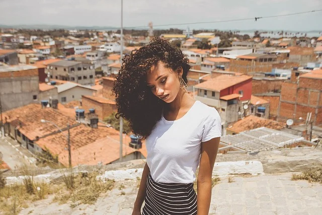 A woman with curly hair wearing a white t-shirt outdoors