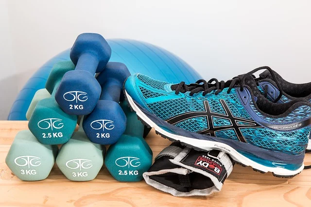 Blue running shoes next to stacked colorful dumbbells and an exercise ball