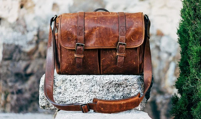 A brown leather messenger satchel bag resting on a stone block