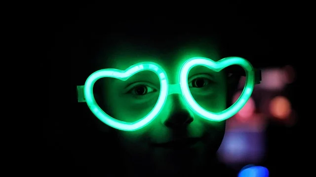 A child wearing glowing green heart-shaped glasses in the dark
