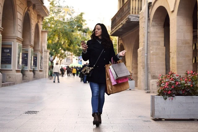 A woman holding shopping bags and looking at her smartphone outdoors