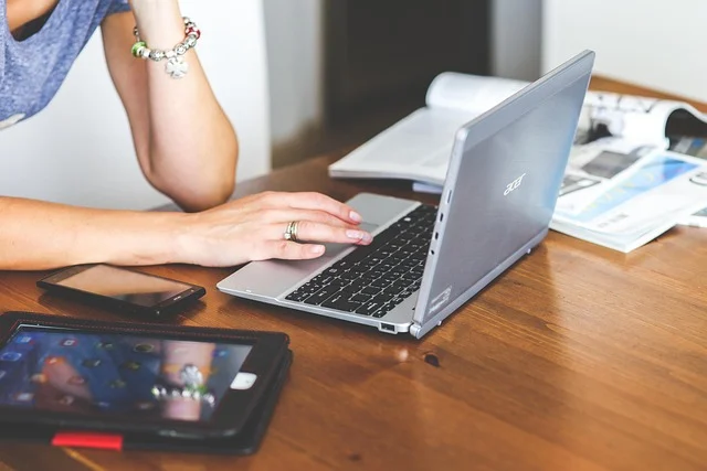 A woman typing on a laptop at a table with devices