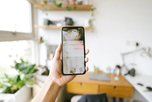 A hand holding a smartphone showing lock screen notifications in a room